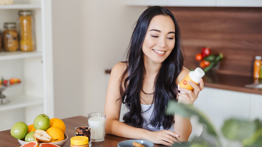 health and wellness products - a woman holding a bottle of supplements with healthy food around her table 